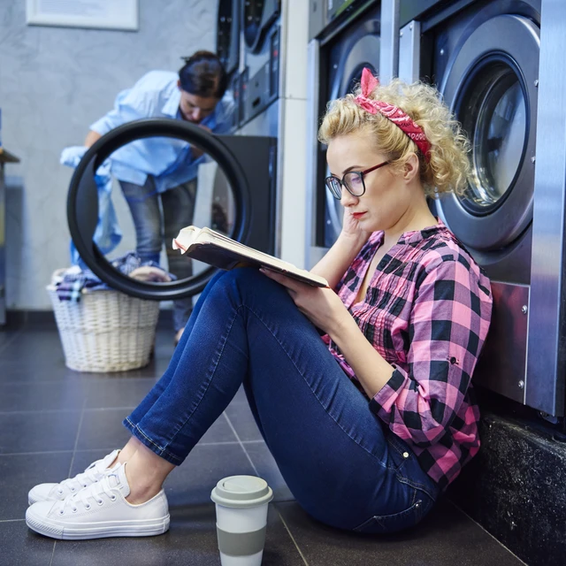 Young woman sitting inside a laundromat and reading a book