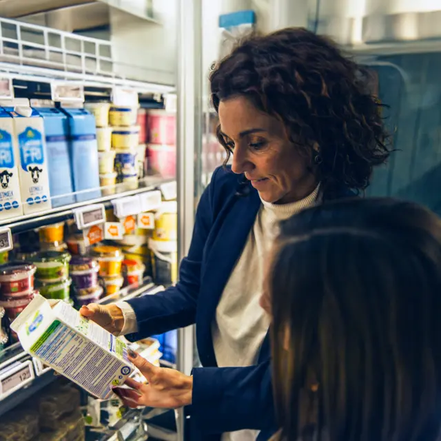 Consumer in supermarket checking the ingredient list of a plant-based drink product 