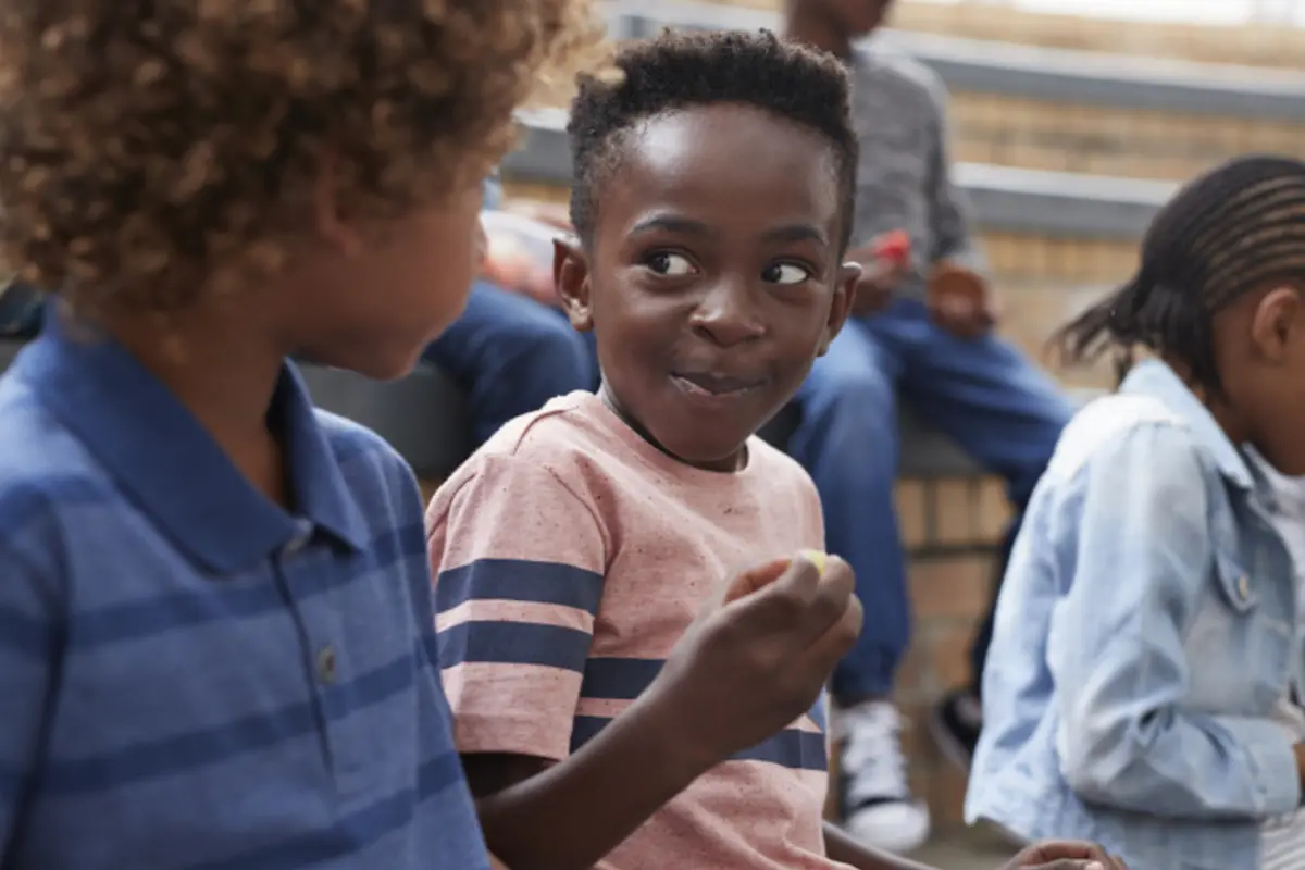 kid eating a snack while sitting with his friend