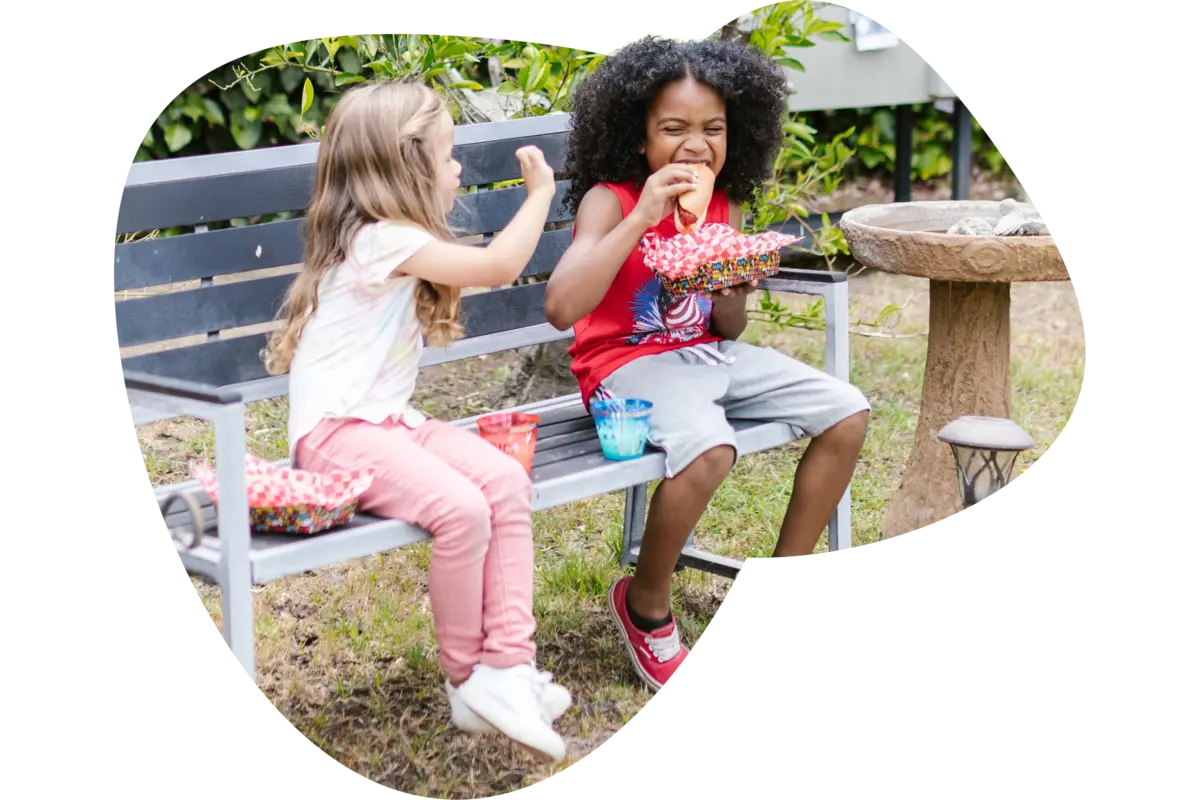 Kid enjoying plant-based sausage with a friend